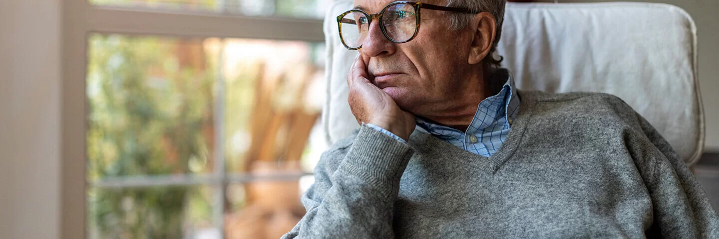 Ein älterer Mann mit Prostatakrebs steht vor dem Fenster und blickt besorgt in die Ferne.