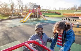 Ein erwachsener Mann und seine Tochter spielen auf einem Klettergerüst auf einem Spielplatz.