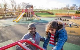 Ein erwachsener Mann und seine Tochter spielen auf einem Klettergerüst auf einem Spielplatz.