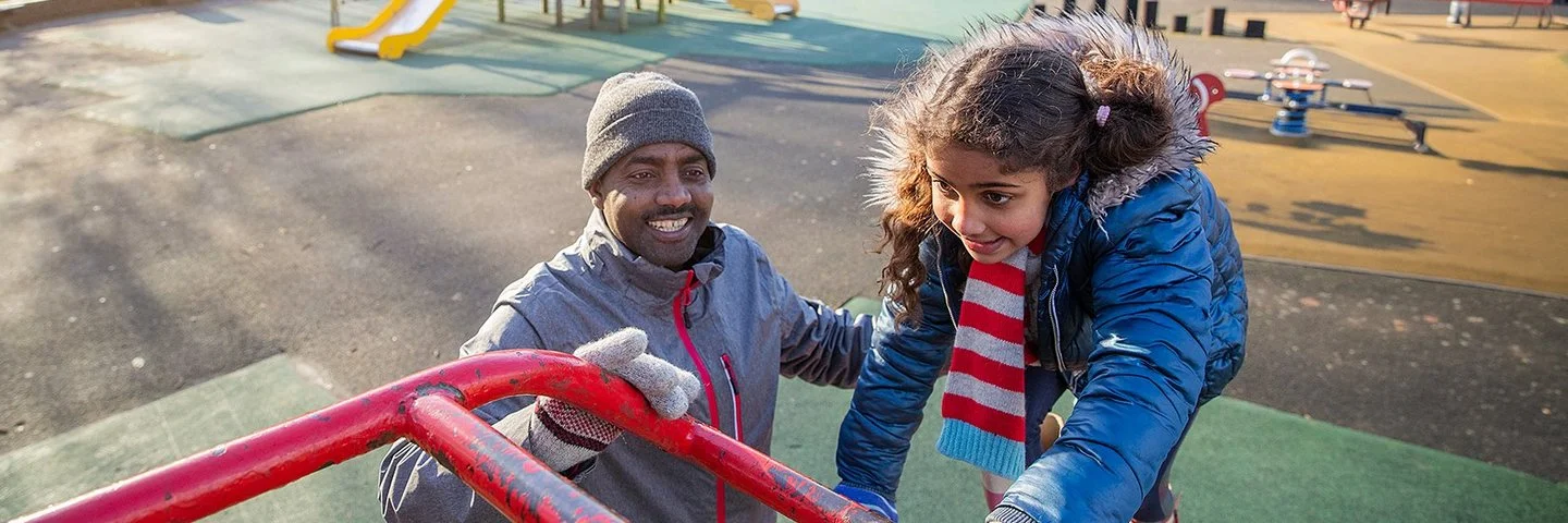 Ein erwachsener Mann und seine Tochter spielen auf einem Klettergerüst auf einem Spielplatz.