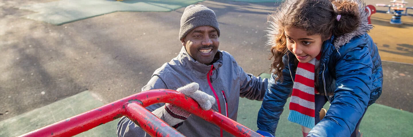 Ein erwachsener Mann und seine Tochter spielen auf einem Klettergerüst auf einem Spielplatz.