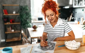 Eine junge Frau malt mit Buntstiften ein Mandala aus.