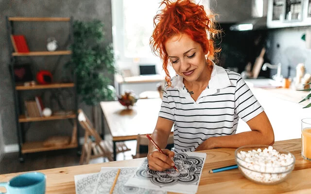 Eine junge Frau malt mit Buntstiften ein Mandala aus.