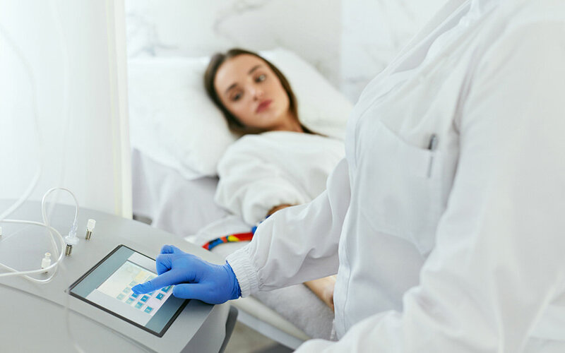 Eine Frau, die auf eine Organspende wartet, liegt in einem Krankenhausbett, während ein Pfleger ein Gerät programmiert.