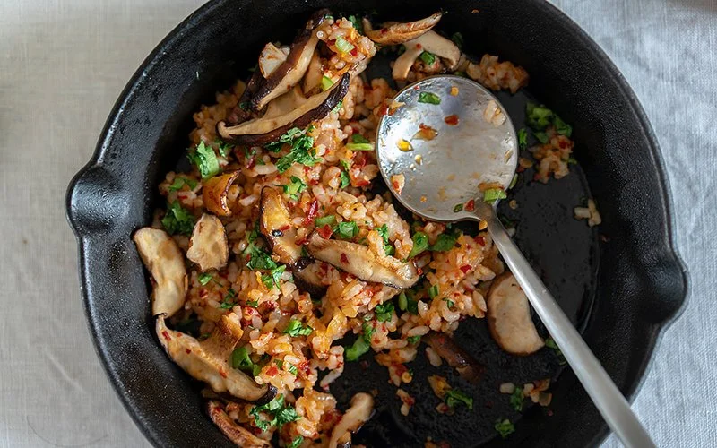 Veganes Pilzgericht mit Steinpilzen, Reis, Chili und Kräutern serviert in einer schwarzen Pfanne.
