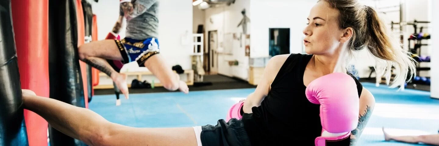 Eine junge Frau trainiert in einem Sportstudio Kickboxen und tritt gegen einen Boxsack.