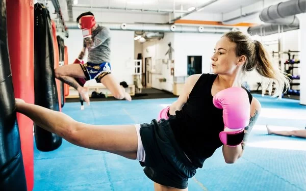 Eine junge Frau trainiert in einem Sportstudio Kickboxen und tritt gegen einen Boxsack.