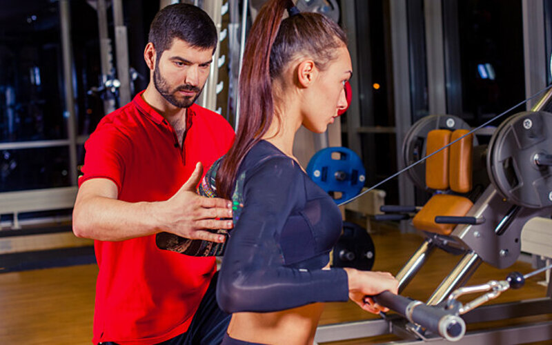 Frau bleibt in Bewegung und trainiert mit Fitnesstrainer an Geräten.