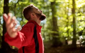 Ein Mann steht im Wald und streckt die Arme weit aus – er kann frei atmen dank Desensibilisierung.