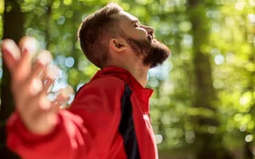 Ein Mann steht im Wald und streckt die Arme weit aus – er kann frei atmen dank Desensibilisierung.