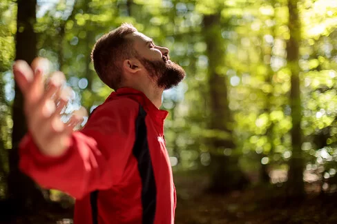 Ein Mann steht im Wald und streckt die Arme weit aus – er kann frei atmen dank Desensibilisierung.