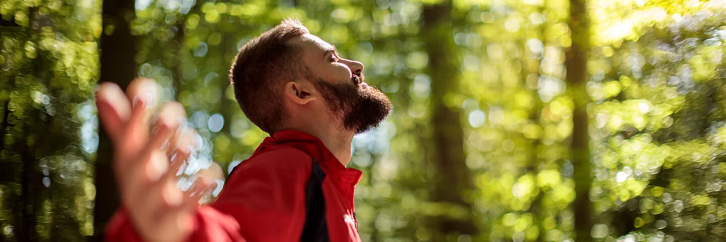 Ein Mann steht im Wald und streckt die Arme weit aus – er kann frei atmen dank Desensibilisierung.