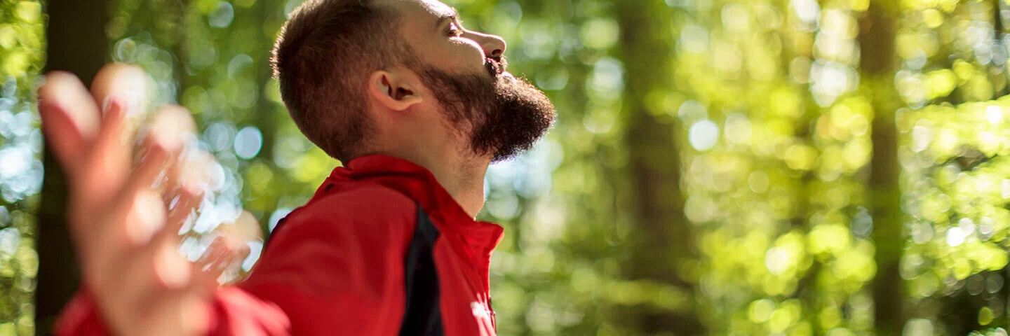 Ein Mann steht im Wald und streckt die Arme weit aus – er kann frei atmen dank Desensibilisierung.