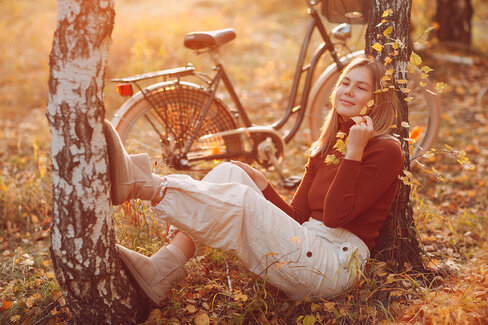 Eine junge Frau sitzt entspannt in einem Park, neben ihr steht ihr Fahrrad.