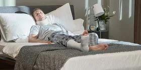 Ein Mann mit Gips am Bein liegt im Bett. Die AOK zahlt Versicherten Krankengeld.