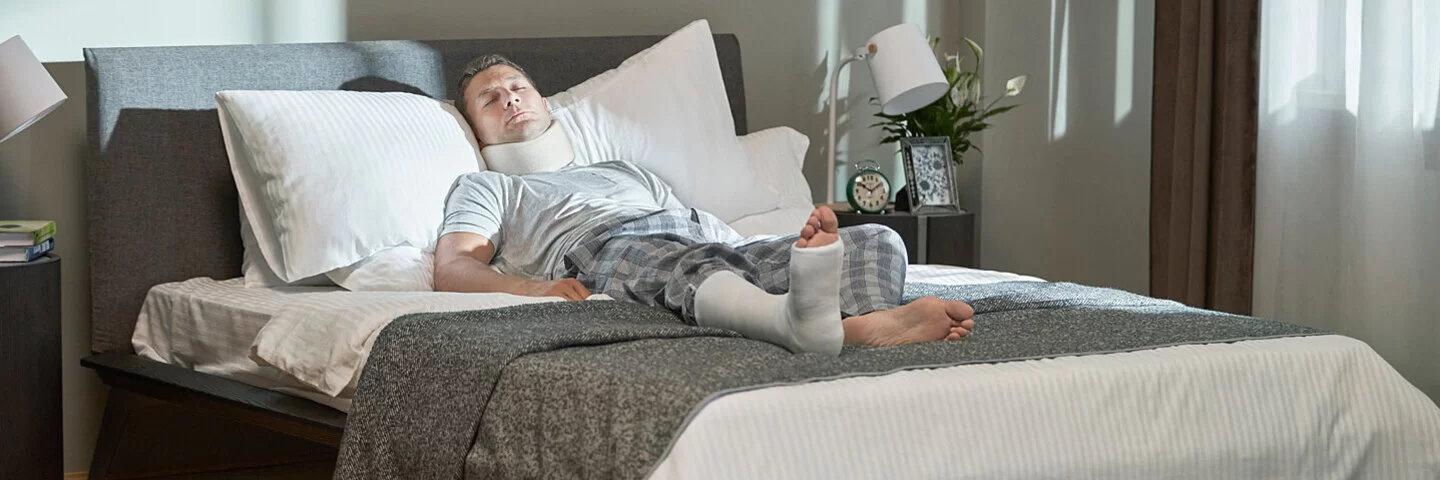 Ein Mann mit Gips am Bein liegt im Bett. Die AOK zahlt Versicherten Krankengeld.