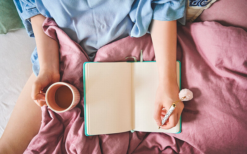 Frau sitzt im Bett und schreibt Tagebuch.
