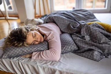 Eine Frau liegt mit geschlossenen Augen auf dem Bauch im Bett.