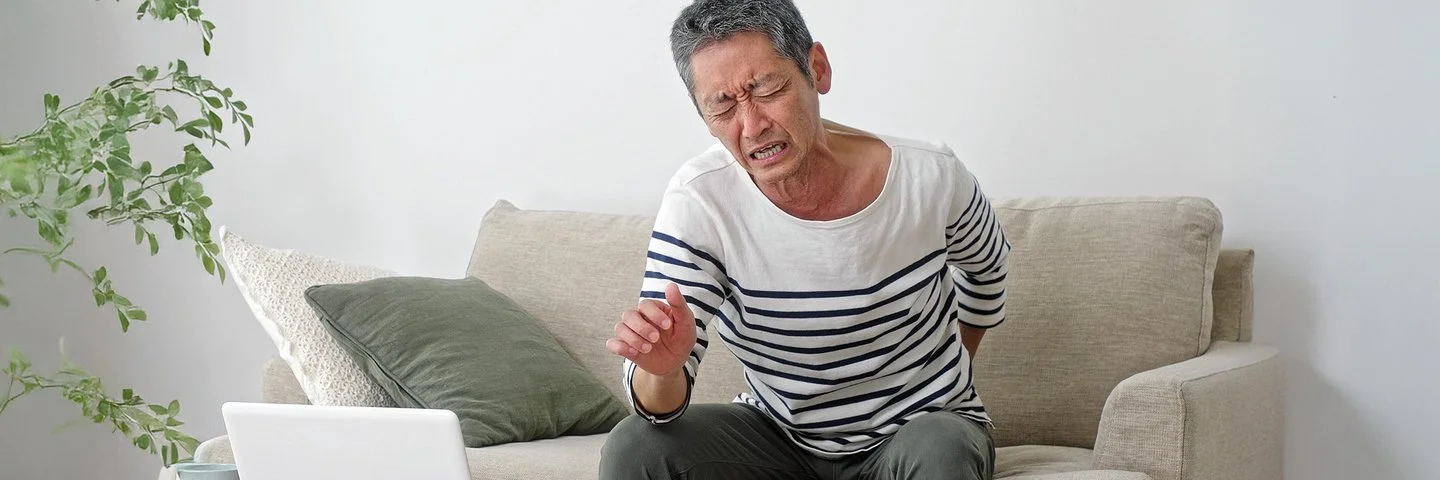 Ein älterer Mann sitzt auf dem Sofa und hält sich den schmerzenden Rücken.