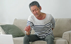 Ein älterer Mann sitzt auf dem Sofa und hält sich den schmerzenden Rücken.