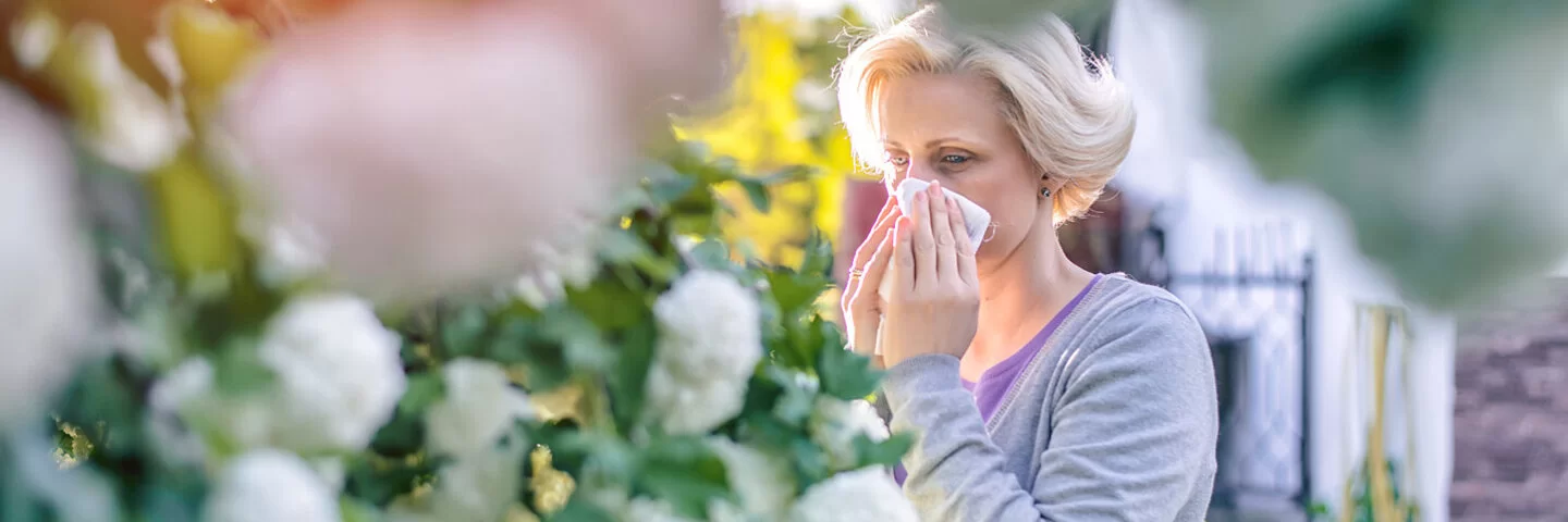 Frau mit einer Pflanzenallergie niest in ihrem Garten wegen der Pollen.