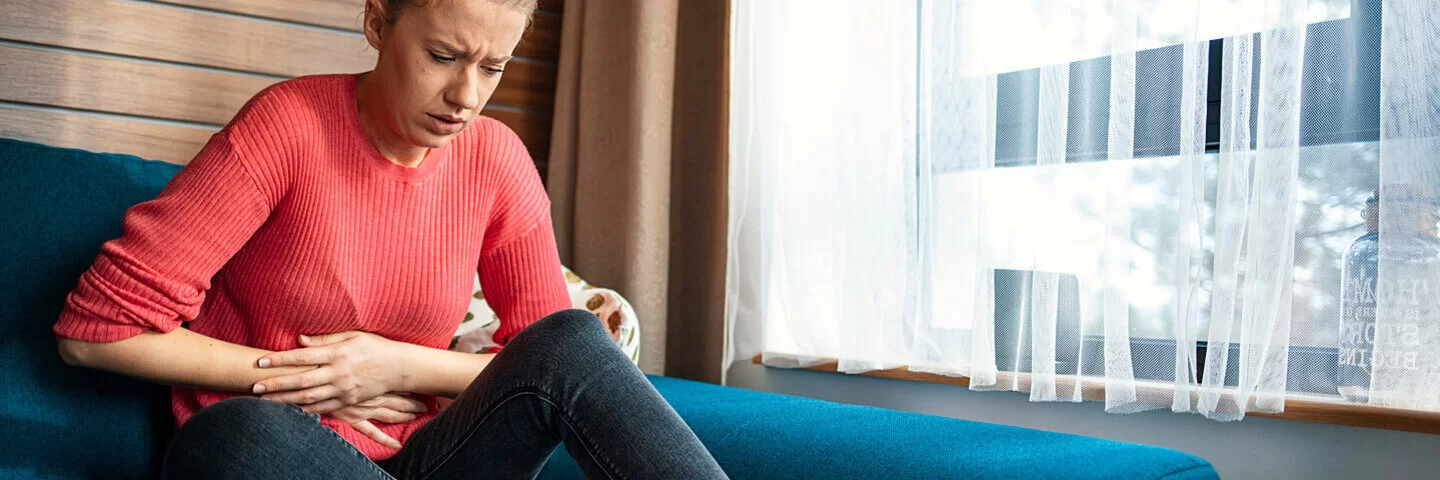 Eine junge Frau sitzt auf der Couch und hat Endometriose-Beschwerden.