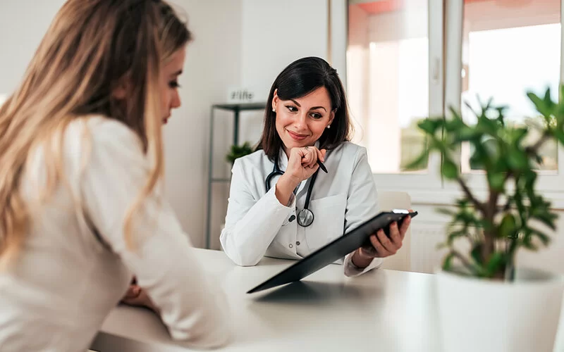 Eine Ärztin hält ein Klemmbrett in der Hand und erklärt ihrer Patientin Untersuchungsergebnisse.