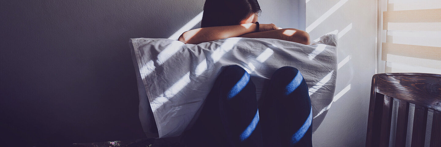 Ein Mädchen, das unter den Symptomen eines Traumas leidet, sitzt auf dem Bett und hat den Kopf in die Arme gelegt.