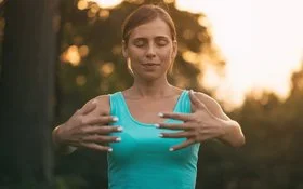 Junge Frau steht draußen im Park und führt Qigong-Übungen durch