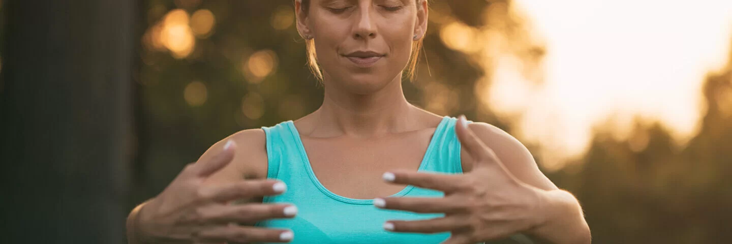 Junge Frau steht draußen im Park und führt Qigong-Übungen durch