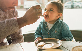 Vater reicht seinem Baby Essen und versucht so, es an feste Nahrung zu gewöhnen