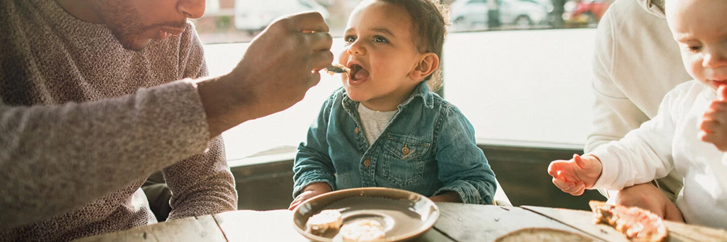 Vater reicht seinem Baby Essen und versucht so, es an feste Nahrung zu gewöhnen