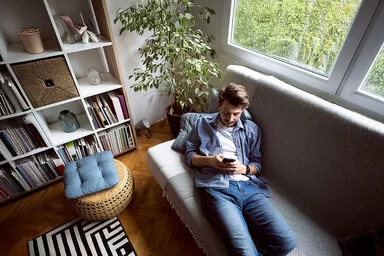Ein Mann liegt auf einem Sofa und blickt auf sein Handy.