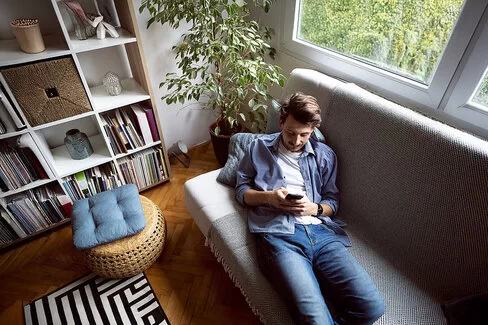 Ein Mann liegt auf einem Sofa und blickt auf sein Handy.
