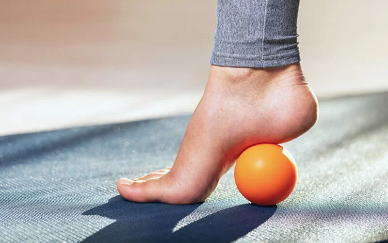 Eine Frau massiert ihre Fußreflexzonen mit einem Ball.