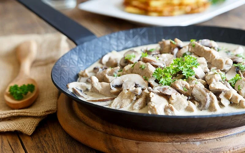 Gusseiserne Pfanne mit Zürcher Geschnetzeltem aus Kalbfleisch und Champignons in cremiger Sauce, garniert mit Petersilie.