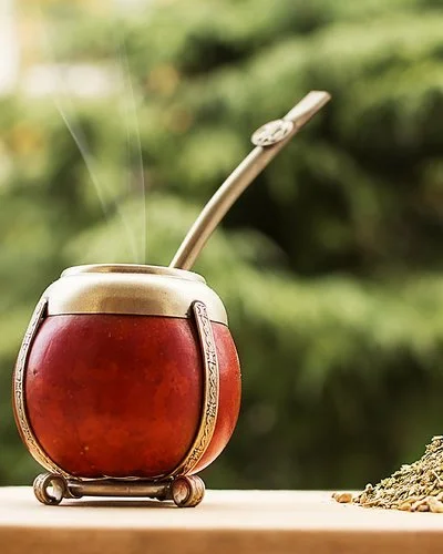 Ein Mate-Teegefäß steht auf einem hölzernen Untergrund, daneben liegen Teeblätter.