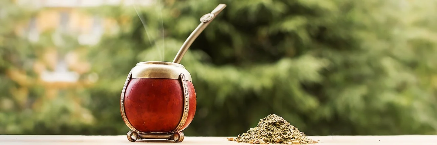 Ein Mate-Teegefäß steht auf einem hölzernen Untergrund, daneben liegen Teeblätter.