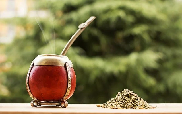 Ein Mate-Teegefäß steht auf einem hölzernen Untergrund, daneben liegen Teeblätter.