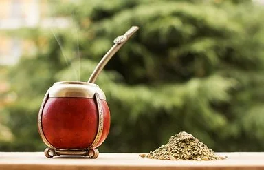 Ein Mate-Teegefäß steht auf einem hölzernen Untergrund, daneben liegen Teeblätter.