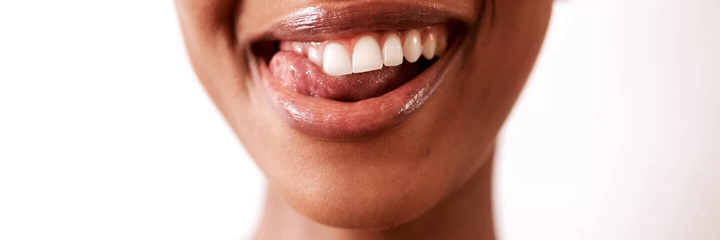 Eine junge Frau streicht mit der Zunge über ihre Zähne.