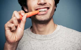 Ein junger Mann beißt von einer Karotte ab.