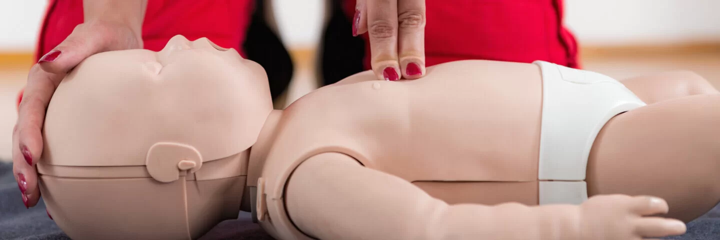 Eine Rettungshelferin drückt auf die Brust einer Babypuppe, um die Erste Hilfe am Baby zu simulieren.