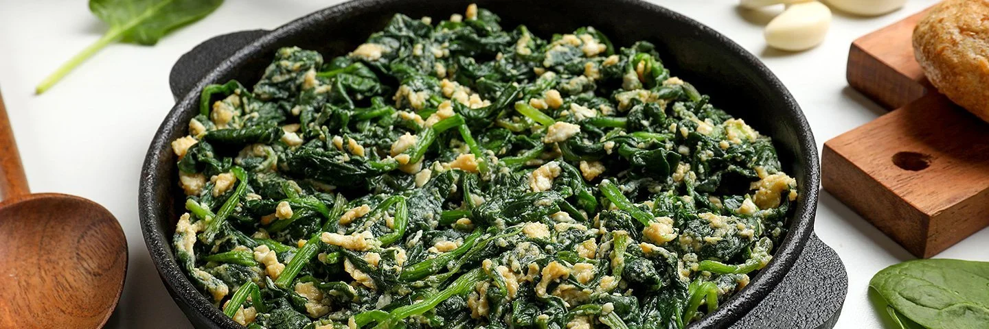 Gedünstete Spinatblätter mit Eiern in einer Pfanne.