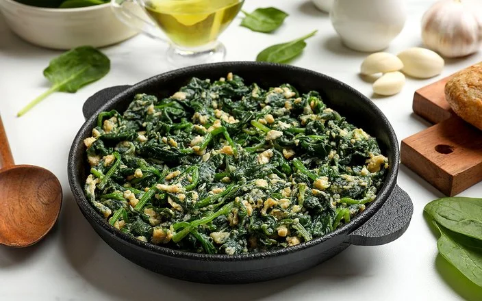 Gedünstete Spinatblätter mit Eiern in einer Pfanne.