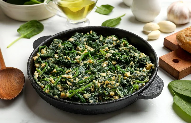 Gedünstete Spinatblätter mit Eiern in einer Pfanne.