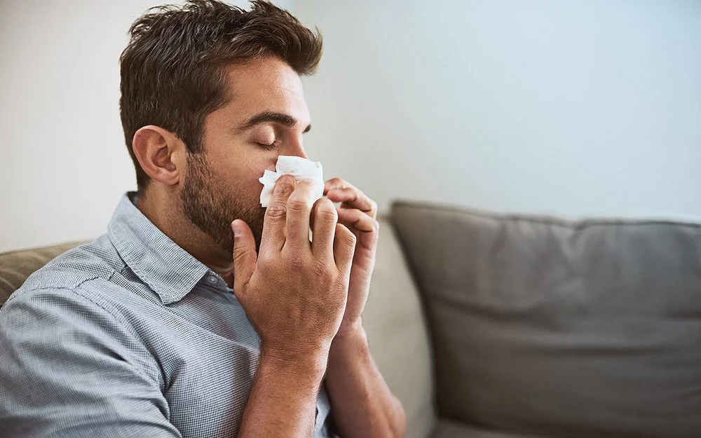 Ein Mann schnäubt sich die Nase wegen einer Hausstaubmilbenallergie.