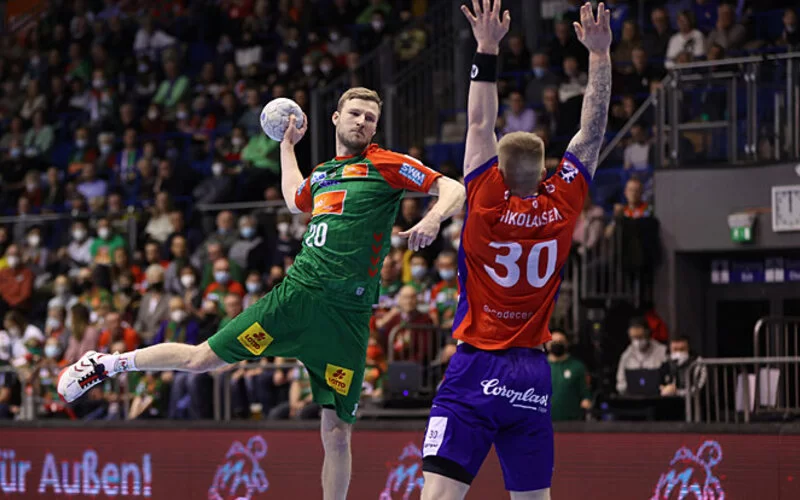 Handball Nationalspieler Philipp Weber hat den Ball in der Hand und setzt auf dem Spielfeld zu einem Schuss an, während ein Spieler der gegnerischen Mannschaft sich ihm in den Weg stellt.