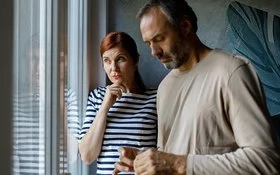 Eine Frau und ein Mann stehen nachdenklich vor einem Fenster.