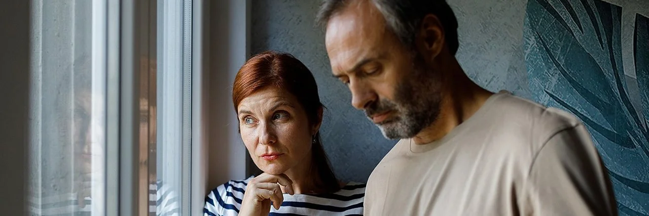 Eine Frau und ein Mann stehen nachdenklich vor einem Fenster.